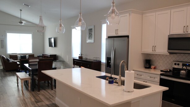 A modern kitchen with white cabinetry, a large island with a sink, and stainless steel appliances. There is a dining area with a table and chairs, and a ceiling fan. - Delightful 3-bedroom house in Bradenton with WiFi, Games, and more #2 of 2 (Bradenton)