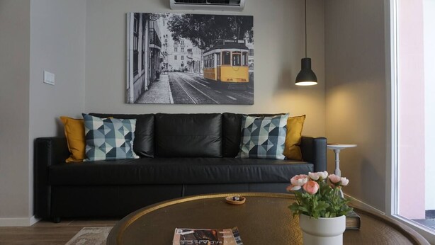 Una sala de estar moderna con un sofá negro, cojines estampados geométricamente, una mesa redonda de centro con una revista, una planta en maceta y un aire acondicionado instalado en la pared.