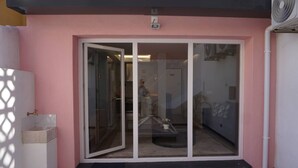 Entrada de hotel con puerta de cristal corredera, un pequeño espacio al aire libre para sentarse y una fuente de agua visible.
