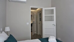 Habitación de hotel con una cama, un equipo de aire acondicionado blanco, una puerta que da a un pasillo y una lámpara.