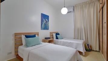 Ein Schlafzimmer mit zwei Betten, einem Bild an der Wand, einer Hängelampe und einem Vorhang.