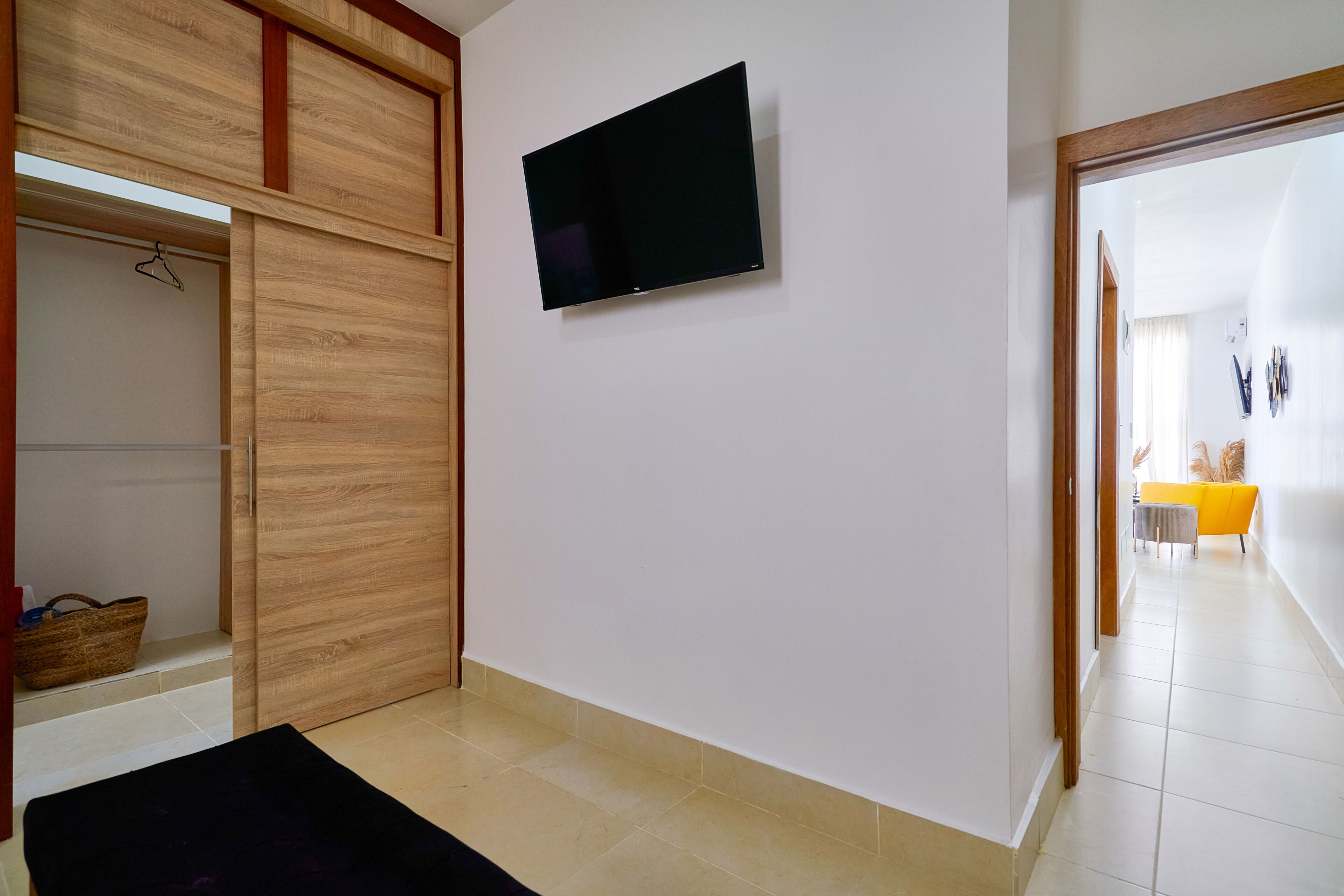 Une chambre moderne avec une armoire en bois à portes coulissantes, un téléviseur à écran plat fixé au mur et une chaise jaune vif en arrière-plan.