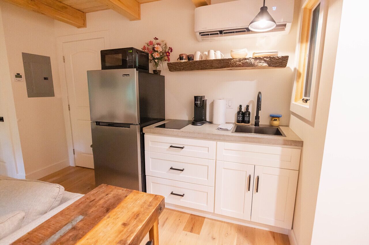 Een compacte keuken met witte kastjes, een roestvrijstalen koelkast, een koffiezetapparaat en een houten tafel.