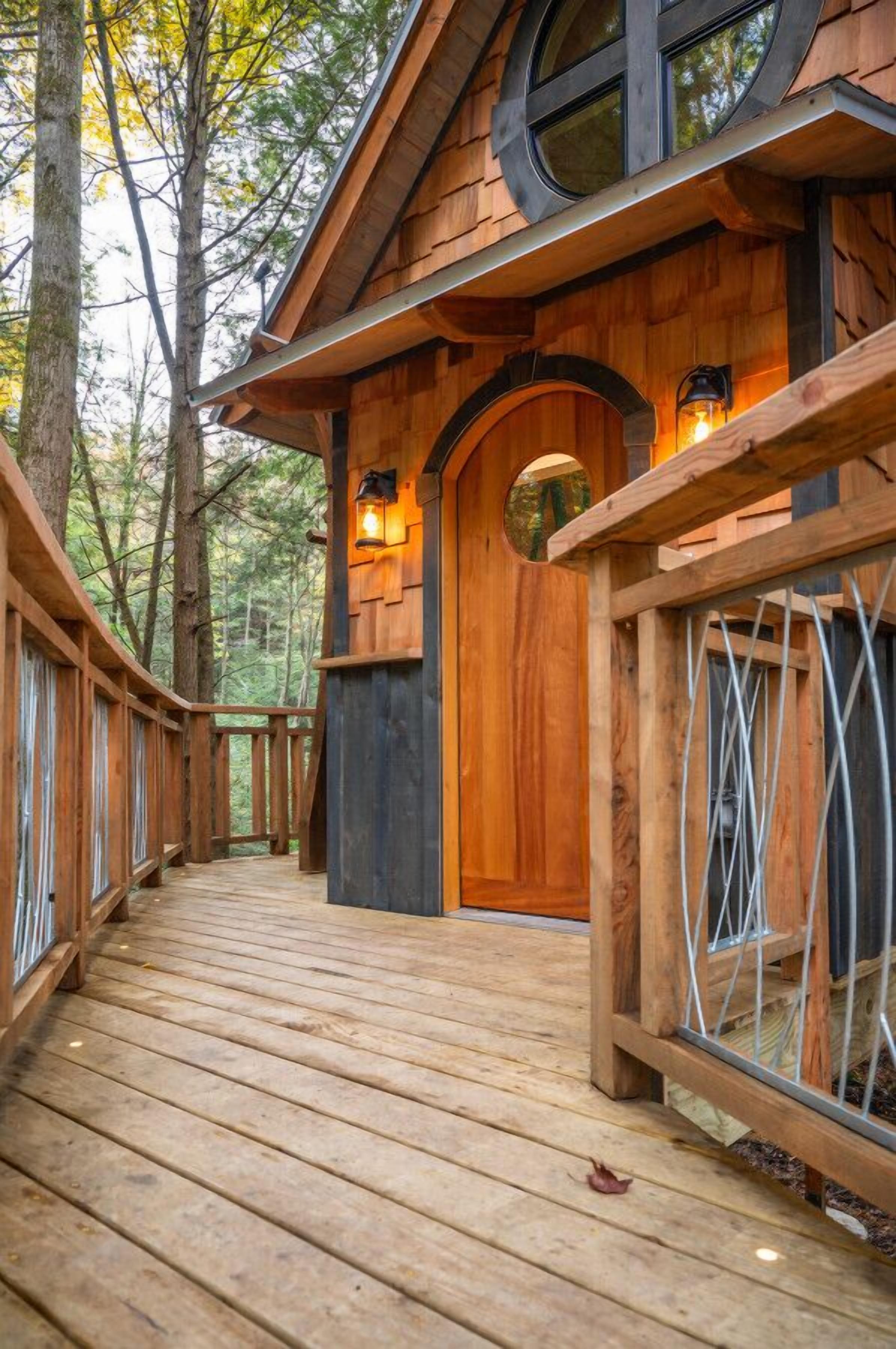 Una cabaña de madera con un porche cubierto de madera que conduce a una puerta circular, rodeada de árboles.