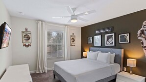 Ein Schlafzimmer mit Bett, Nachttischen, Deckenventilator und Wanddekorationen, darunter 'Wanted'-Poster und ein Poster von Stormtroopern.