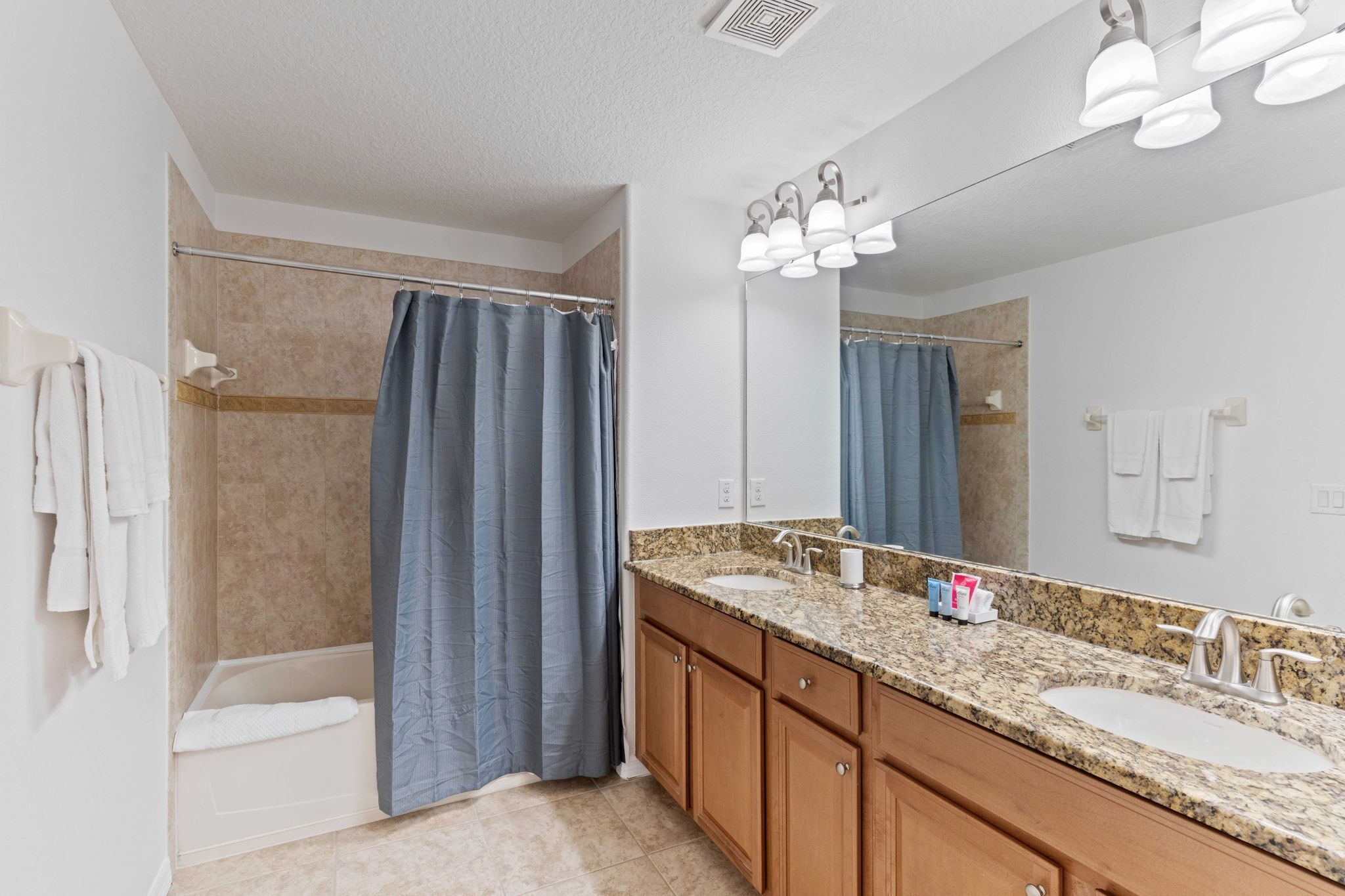 A modern bathroom with a walk-in shower, a large mirror, and a granite countertop with two sinks.