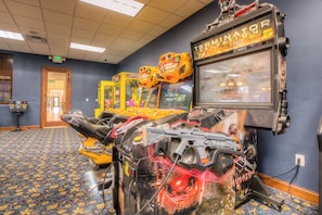 A room with arcade games, a large screen, and a patterned carpet. - 8960 Cat Palm Road (Kissimmee)