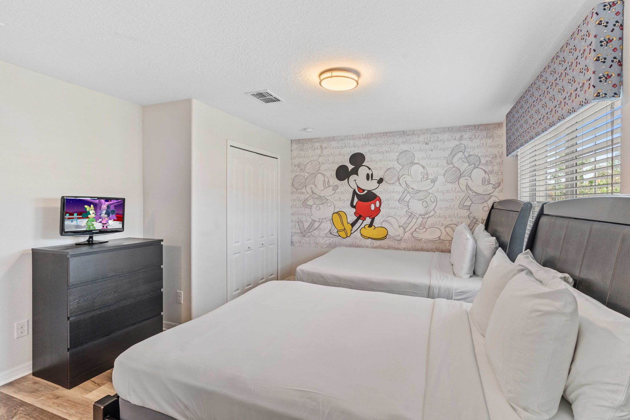 A hotel room with two beds, a television on a dresser, and a Mickey Mouse mural on the wall.