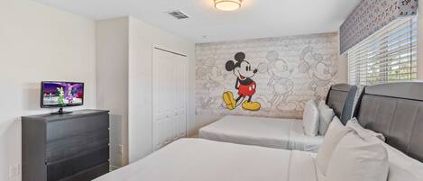 A hotel room with two beds, a television on a dresser, and a Mickey Mouse mural on the wall.