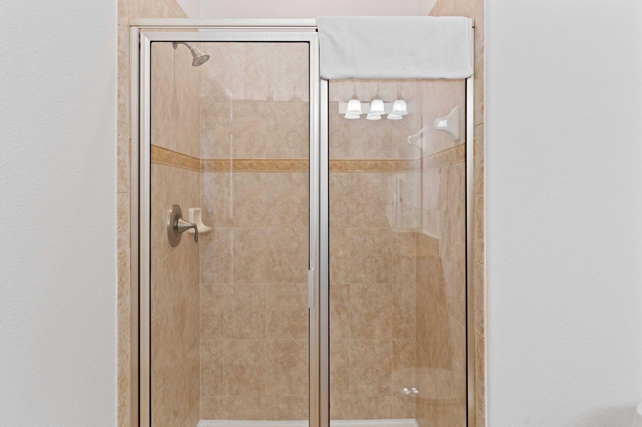 Box de vidro com toalha branca na porta, chuveiro e painel de controle com três botões.