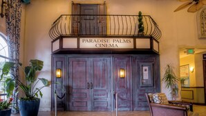Der Eingang zum Paradise Palms Cinema mit einem Schild über den Türen, Zimmerpflanzen und einem Warnhinweis auf dem Boden.