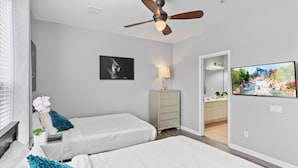 A hotel room with two beds, a ceiling fan, a TV, a lamp, a dresser, and a bathroom visible through an open door. - 5038 Tideview Circle #20 (Orlando)