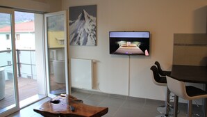 Una sala de estar moderna con televisor montado en la pared, una mesa de centro de madera y un balcón con vistas a edificios.