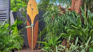 Um portão de madeira com design único, cercado por plantas tropicais exuberantes e uma cerca de madeira.