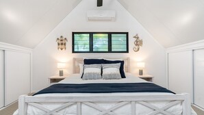 Quarto com uma cama, duas mesas de cabeceira, uma janela e um aparelho de ar condicionado.