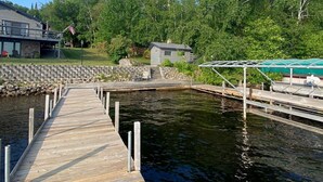 A wooden dock leading to a small docked boat, surrounded by lush greenery and a stone wall.