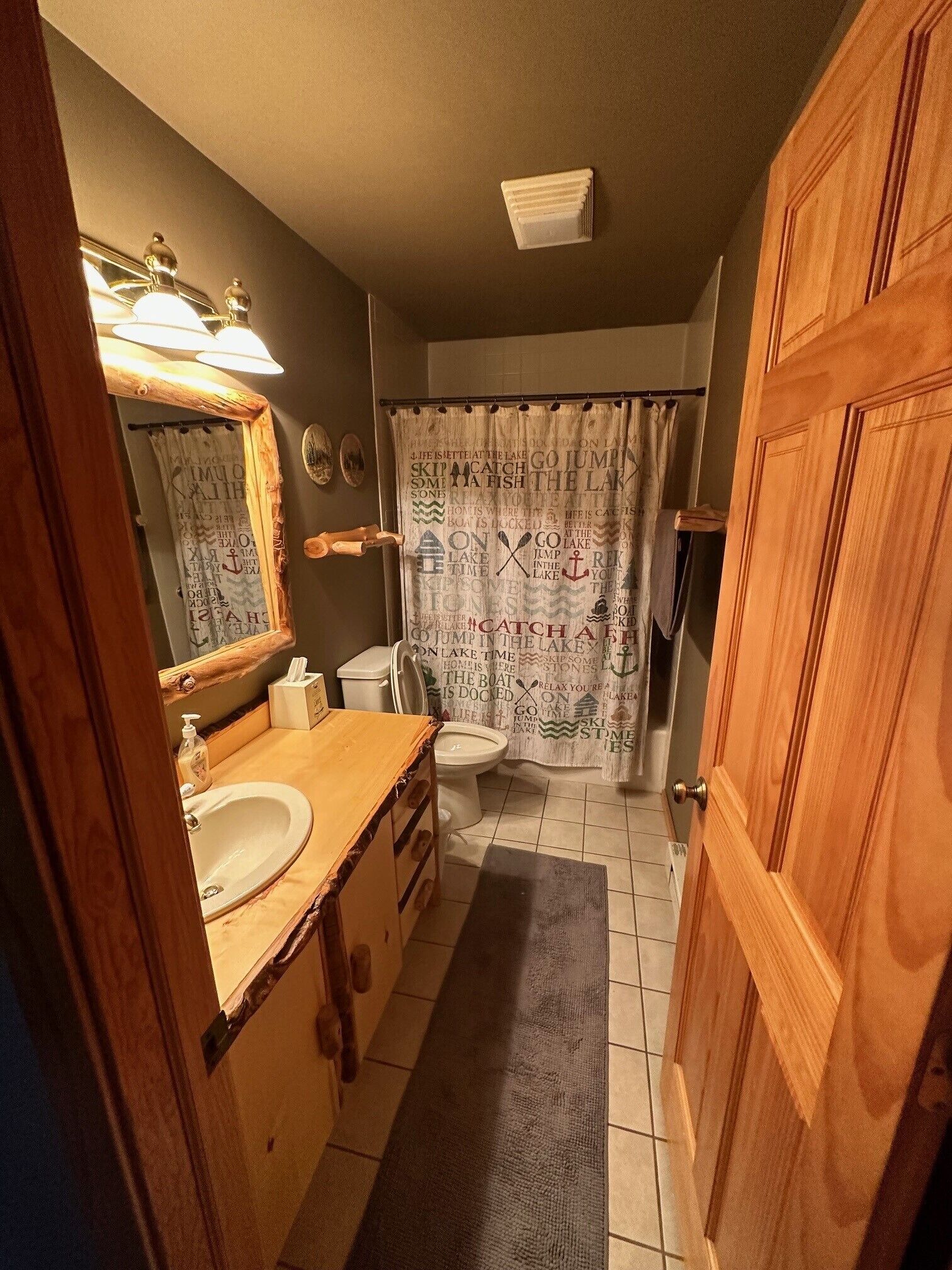 A bathroom with a wooden vanity, a sink, a toilet, and a shower curtain with text.