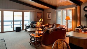 A cozy living room with a leather sofa, a coffee table, and a lamp. There is a large window with a view of the outdoors.