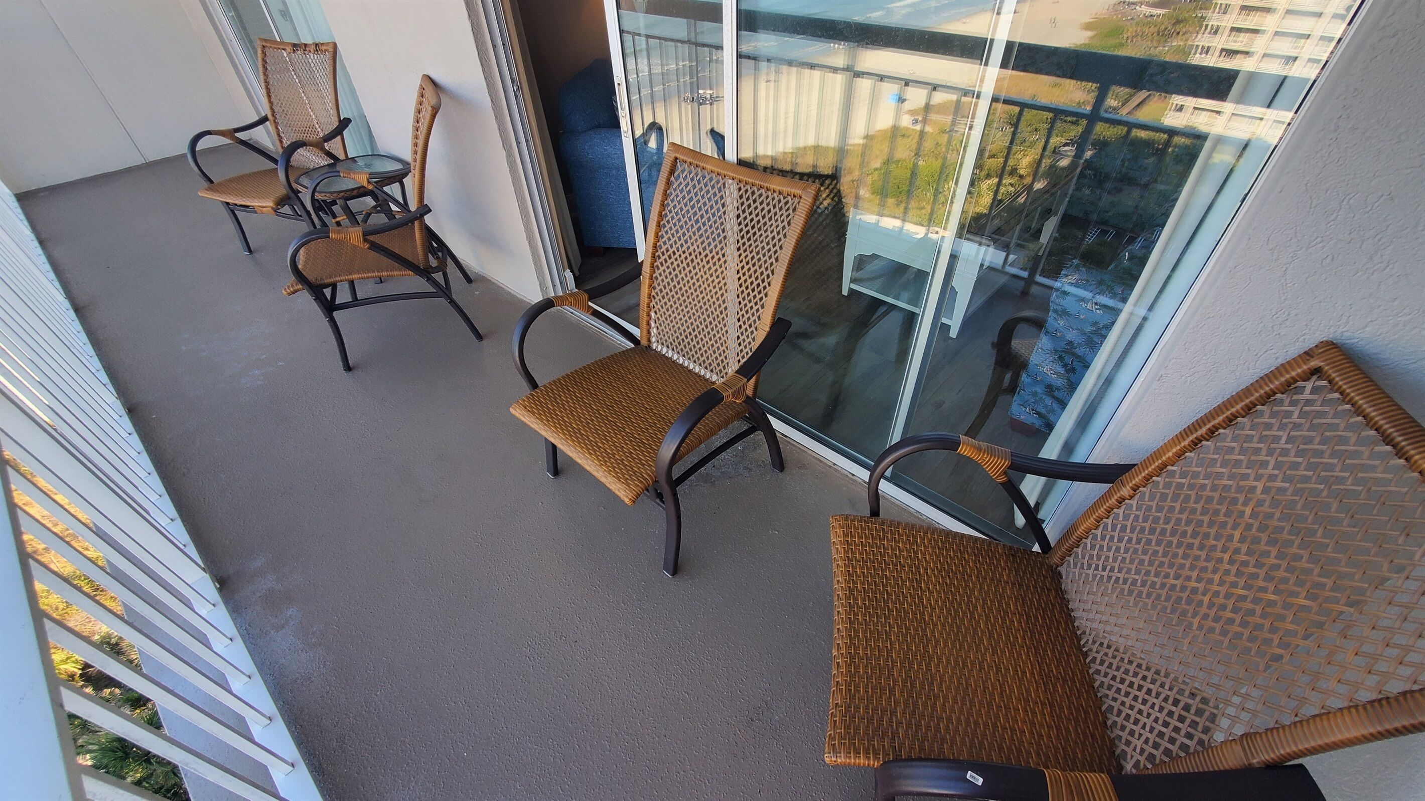 Un balcon avec des fauteuils en osier et une porte vitrée donnant sur une terrasse.