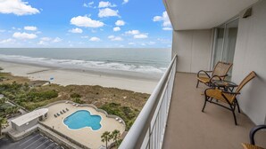 Ein Balkon mit Blick auf Strand und Meer, ein Pool und Korbmöbel.