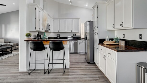 A modern kitchen with white cabinetry, a central island with two bar stools, stainless steel appliances, and a black countertop. - Entire Home in Las Vegas! (Las Vegas)