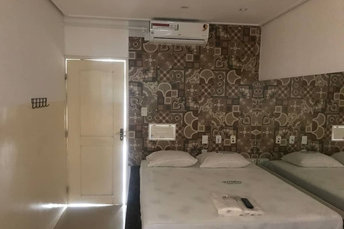 A hotel room with a large bed, a wall-mounted air conditioner, and patterned wallpaper.