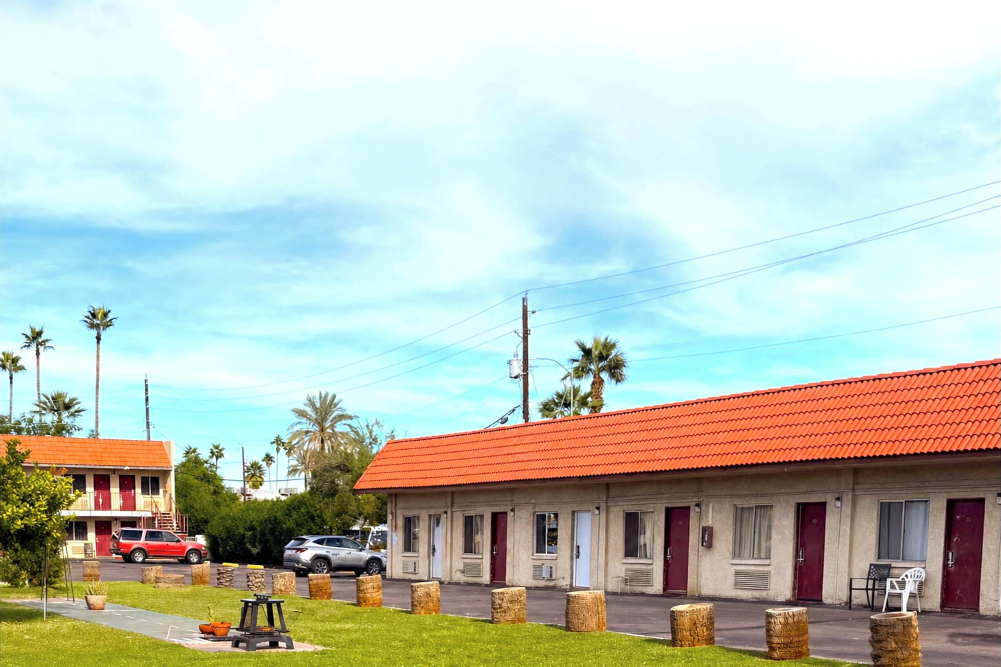 A motel with a red roof, multiple rooms, and a parking area with cars.