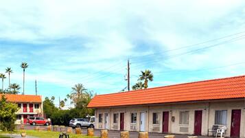 A motel with a red roof, multiple rooms, and a parking area with cars.