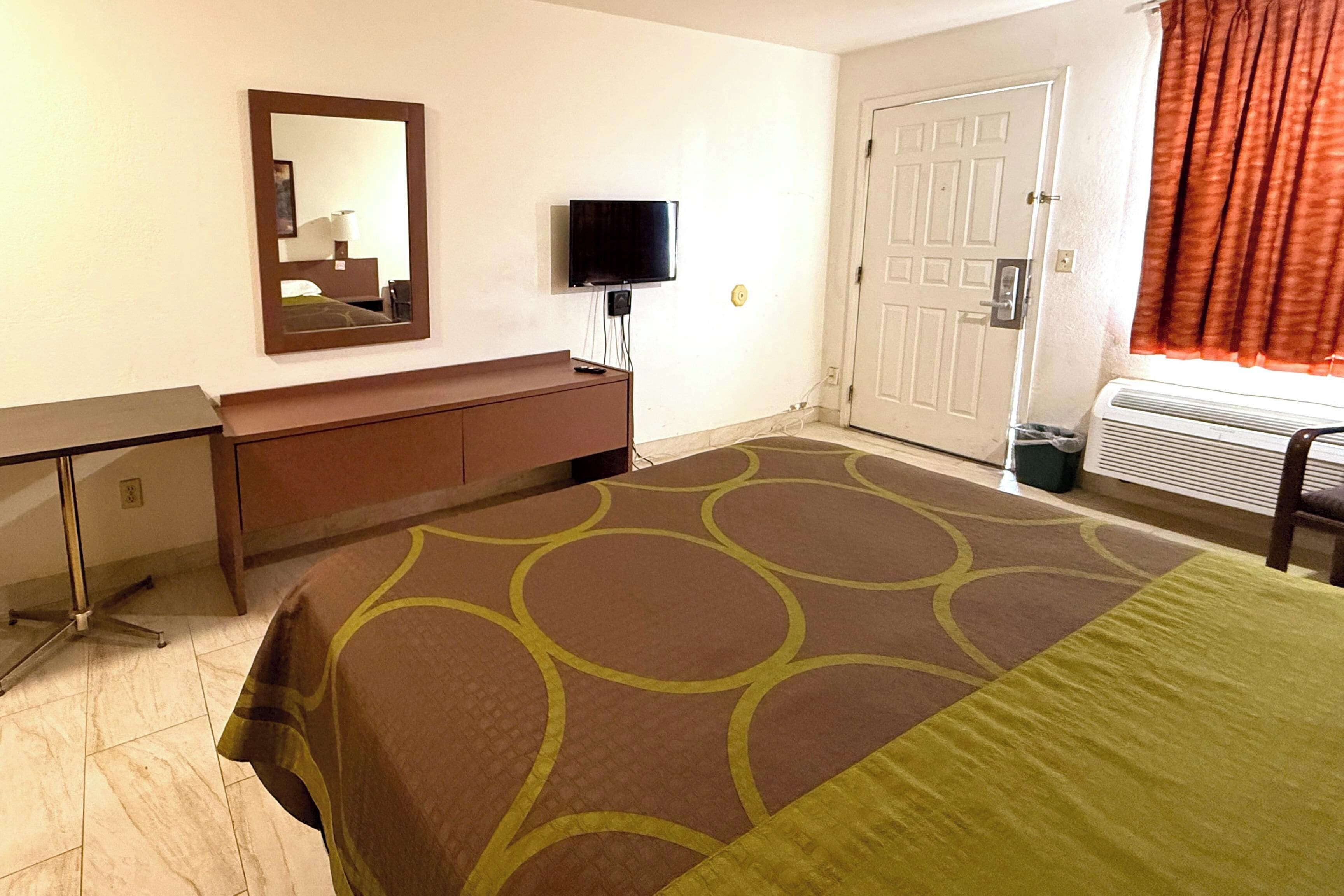 Ein Hotelzimmer mit Bett, Schreibtisch, Spiegel, Fernseher und einer Tür.