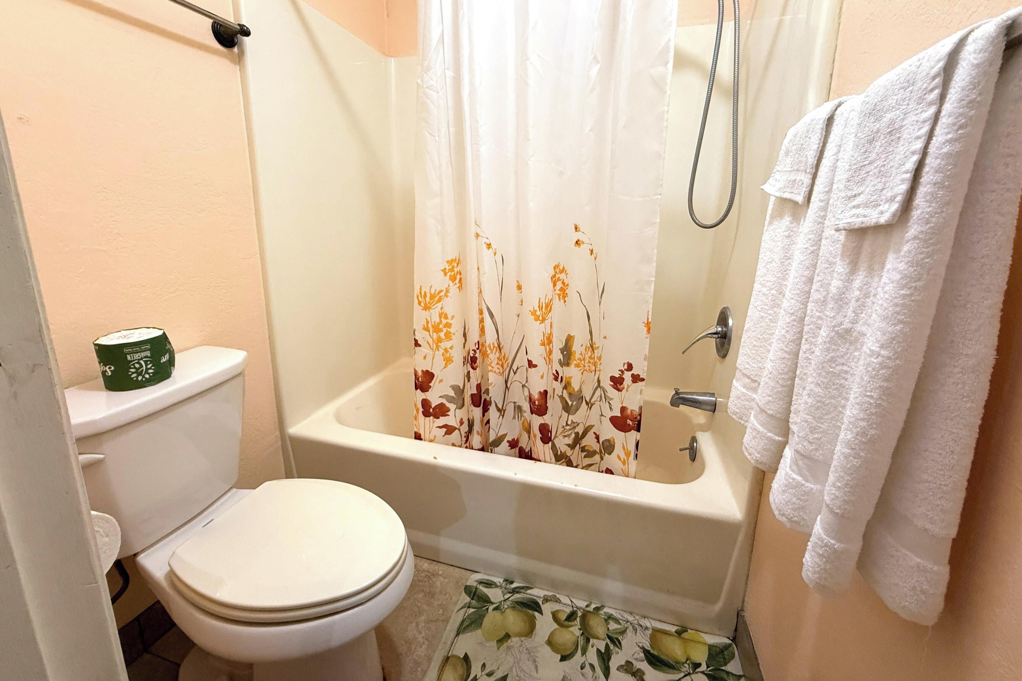 Een badkamer met toilet, een douche met bloemen gordijn en een handdoekrek.