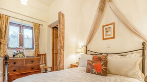 Een slaapkamer met een bed, een kaptafel, een stoel, een nachtkastje, een lamp en een raam met gordijnen.