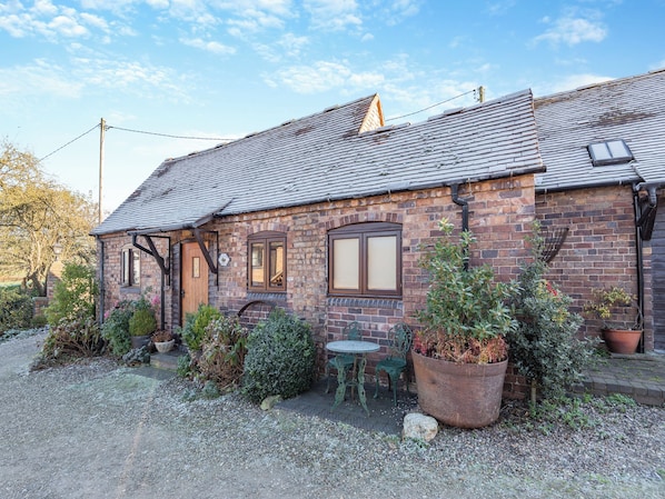 A brick house with a tiled roof, a front door, and a small patio with potted plants and a table.