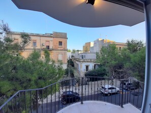 A balcony with a view of a street, buildings, and parked cars.
