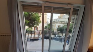 Une pièce dotée d’une porte-fenêtre coulissante donnant sur un balcon. Le balcon est muni d’une rambarde en métal et offre une vue sur la rue et les bâtiments environnants.
