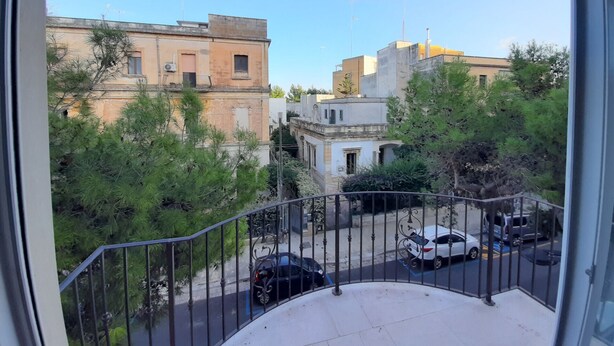 Un balcon donnant sur une rue, des voitures garées et des immeubles.