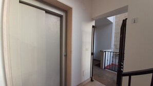 Un couloir avec une porte fermée, un escalier menant à l’étage supérieur et un petit espace extérieur doté d’une rambarde.