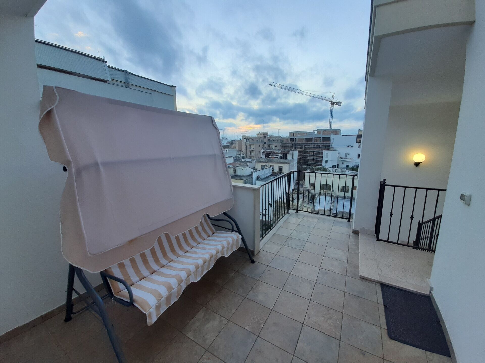 Un balcon doté d’un espace salon couvert, offrant une vue sur le paysage urbain, avec une grue de construction visible au loin.