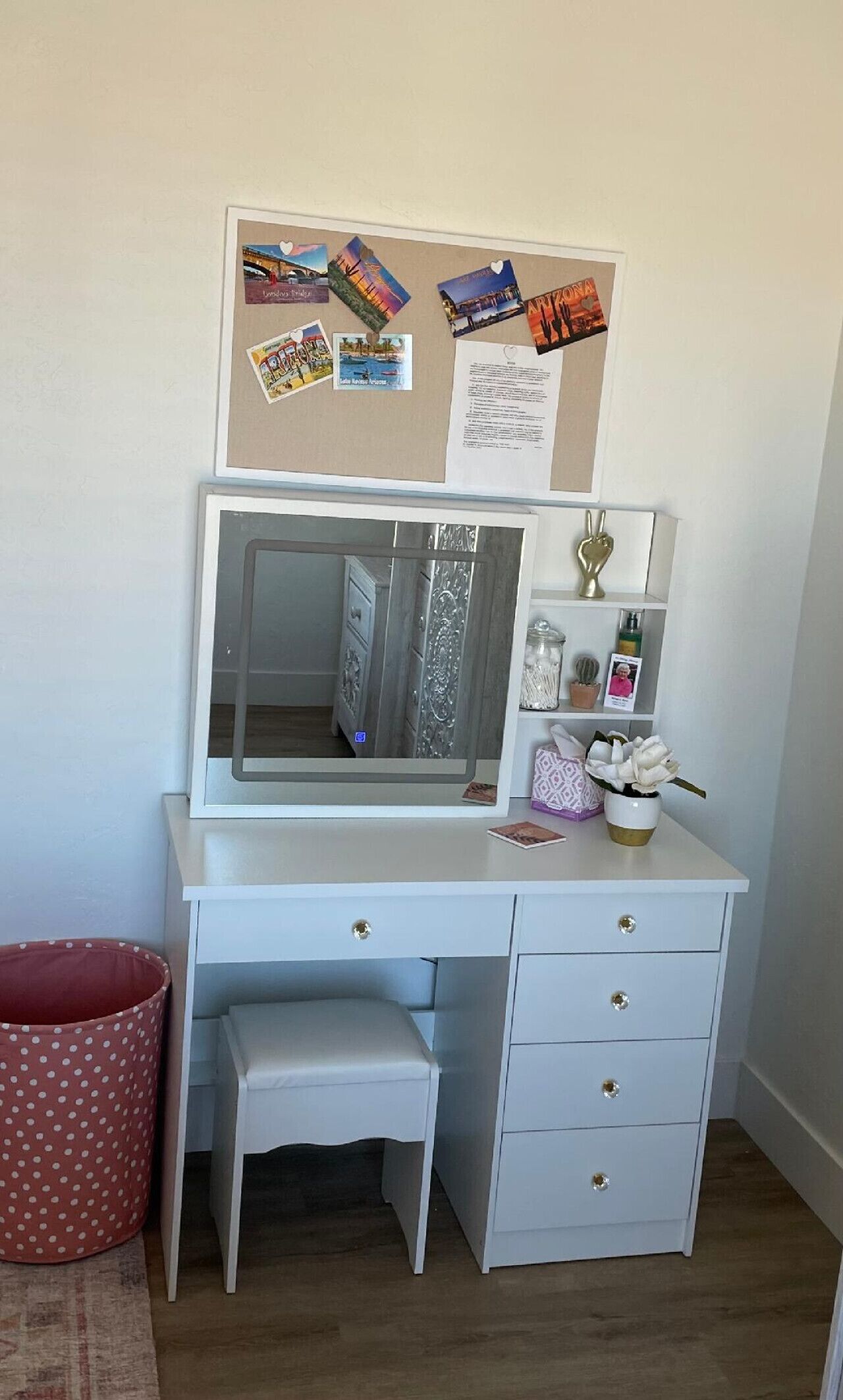Een wit bureau met een spiegel, lades en een prikbord met reis foto’s en notities.