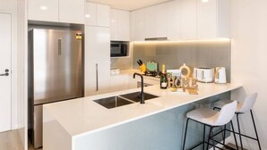 Une cuisine moderne avec des meubles blancs, des appareils en acier inoxydable et un îlot central doté de tabourets de bar.