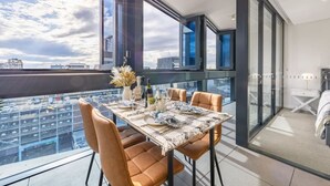 Un coin repas avec une table dressée pour quatre personnes, de grandes fenêtres et une vue sur la ville.