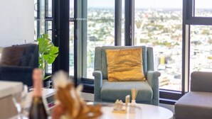 A modern living room with large windows, a dining table set with plates and glasses, and a sofa with a yellow pillow.