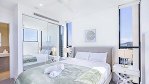 A modern hotel room with a large bed, a bedside table, a mirror, and a view of the city through a large window. - Conveniently located 2BR apt w/ rooftop pool @Milt (Milton)