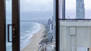 Une vue depuis une chambre d’hôtel, avec une grande fenêtre donnant sur une plage et des immeubles de grande hauteur.