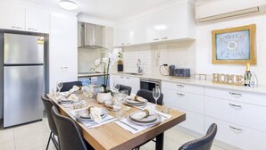 A modern kitchen with white cabinetry, a dining table set for four, and a decorative clock on the wall.