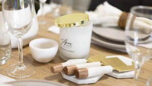 A table set with wine glasses, a white candle, and a white container with a gold lid.