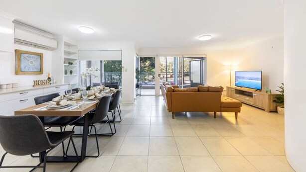 A modern living room with a dining area, a sofa, a TV, and a balcony with a view.