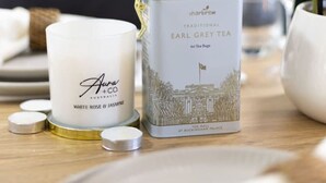 A tea bag container and a candle on a wooden surface.