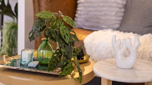 Un salon chaleureux avec un canapé en cuir marron, une table basse ronde en bois agrémentée d’une plante et d’objets décoratifs, un vase blanc et une lampe.
