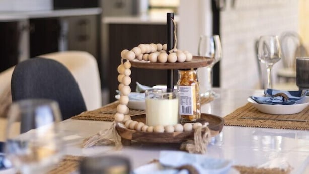 Une table à manger décorée avec un centre de table composé de perles en bois, d’une bougie et d’une bouteille de miel.