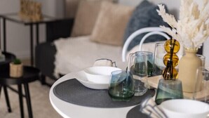A dining area with a round table set for two, featuring a white plate, a glass, and a vase with dried flowers.